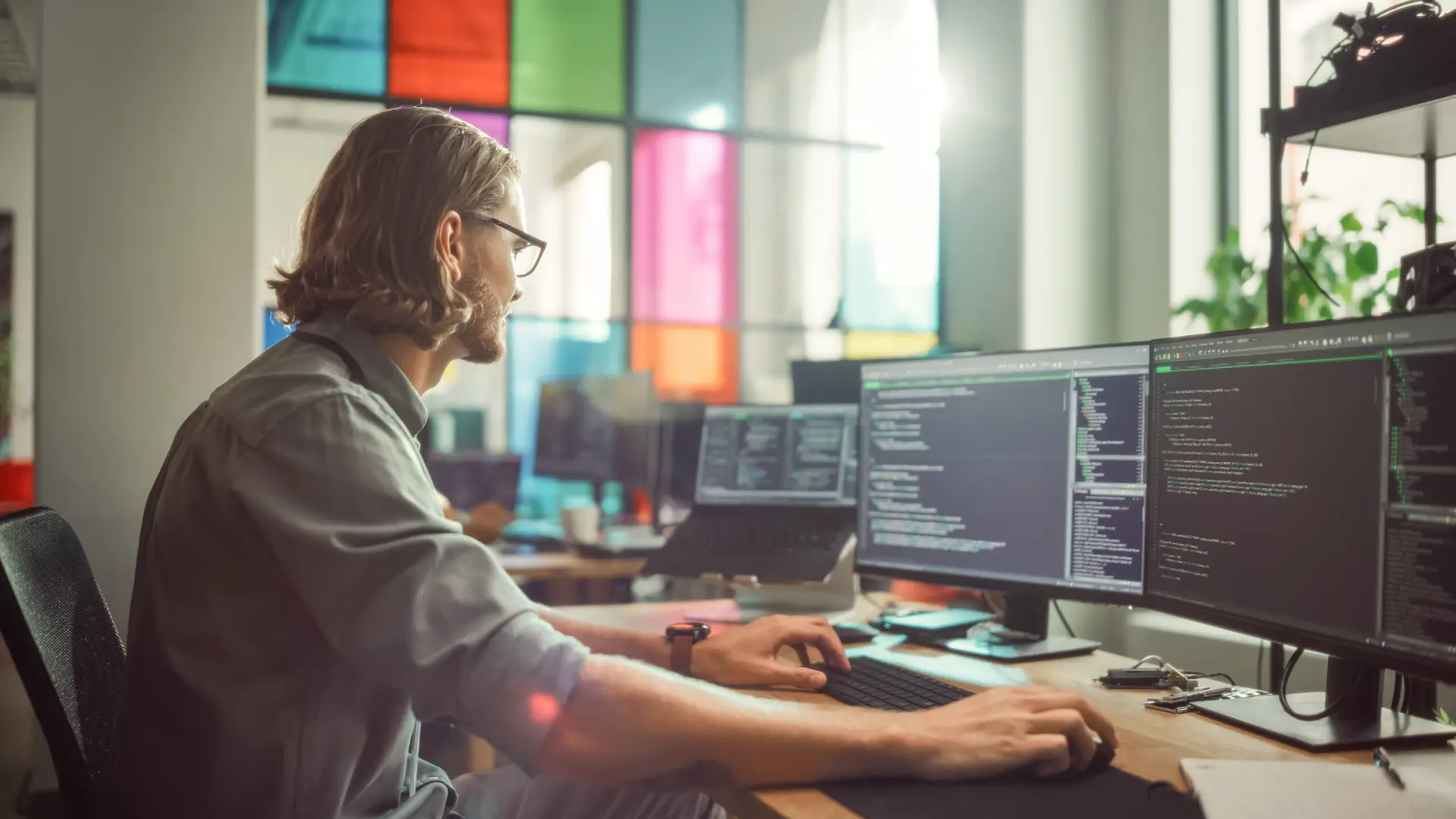 Professional Male Programmer Writing Code on Desktop Computer With Multiple Displays in Stylish Office. Caucasian Man Does Data Scraping For Artificial Intelligence Innovative Start-Up.